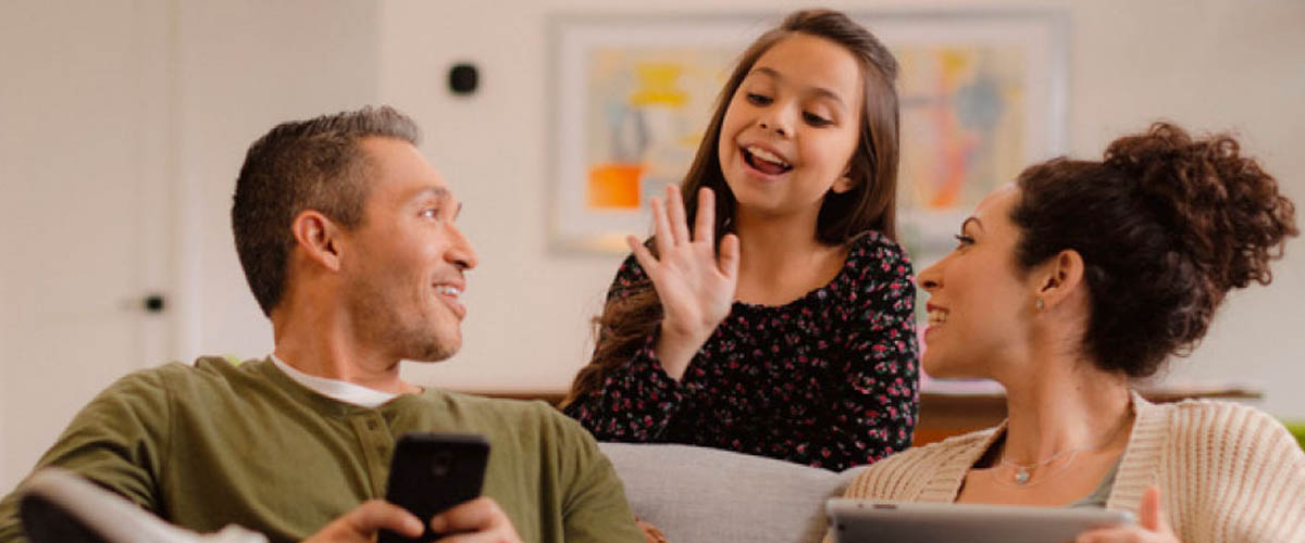 A mother, father and young daughter who reside in Arizona chatting in their home.