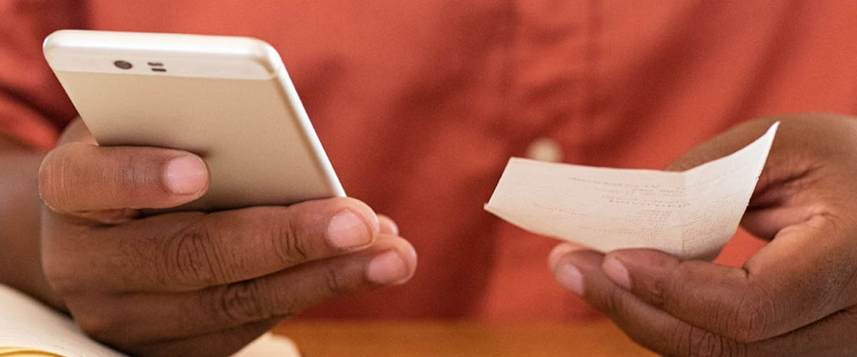 A woman in an orange shirt reviews a receipt and her phone.