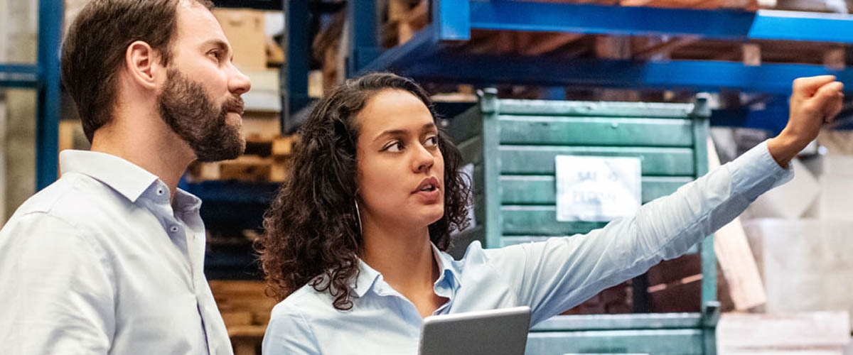 Two colleagues review products and large equipment in their warehouse.