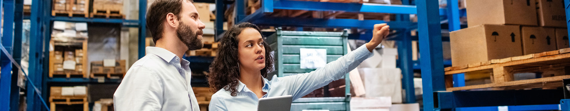 Two colleagues review products and large equipment in their warehouse.