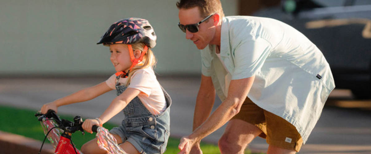 A dad in sunglasses teaches his young daughter how to ride a bike in Arizona, enjoying one of the 330 days of sunshine in the sate.